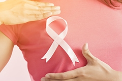 A woman wearing a dark pink t-shirt performing a breast self-exam with a breast cancer awareness ribbon between her hands