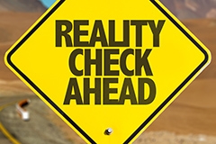 A yellow road sign reading: REALITY CHECK AHEAD