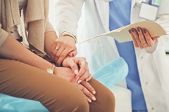 A doctor holding a female patient's hand while reviewing a medical file with her