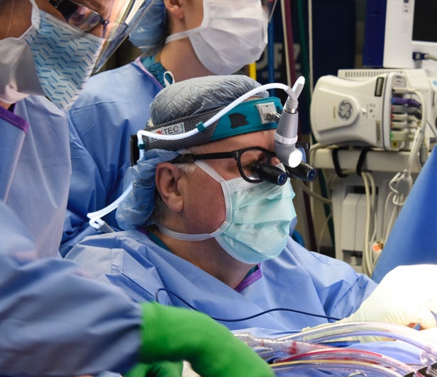 A McLeod doctor in scrubs performing surgery with two nurses assisting behind him