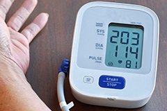 A person's hand next to a blood pressure monitor showing a reading of 203 over 114