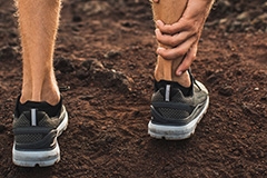 A man wearing grey running shoes grabbing the back of his ankle