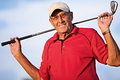 An older man wearing a golfing polo and carrying a golf club over his shoulder