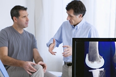 A doctor explaining knee replacement surgery to a man while an x-ray is also visible in the foreground