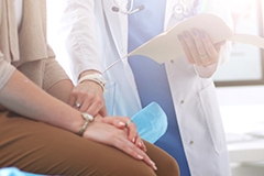 A doctor holding a female patient's hand while reviewing a medical file with her