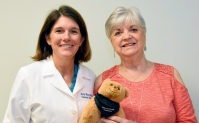 Linda Brown and Dr. Amy Murrell posing with a small teddy bear called a Breast Bear which helps comfort breast cancer patients