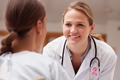 A doctor wearing a stethoscope and a breast cancer awareness ribbon talking to a patient