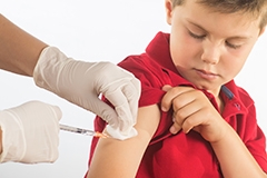 A boy wearing a red shirt getting a shot in the arm