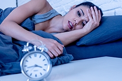 A woman in distress staring at a clock while in bed