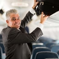 A man in a suit putting his bag in an overhead bin on an airplane