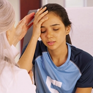 A young woman holding her head in pain as a doctor examines her