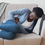 An African-American woman on a couch clutching her pelvis in pain
