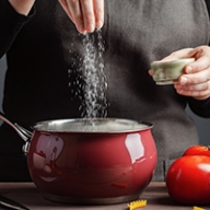 A cook sprinkling a good deal of salt into a cooking pot